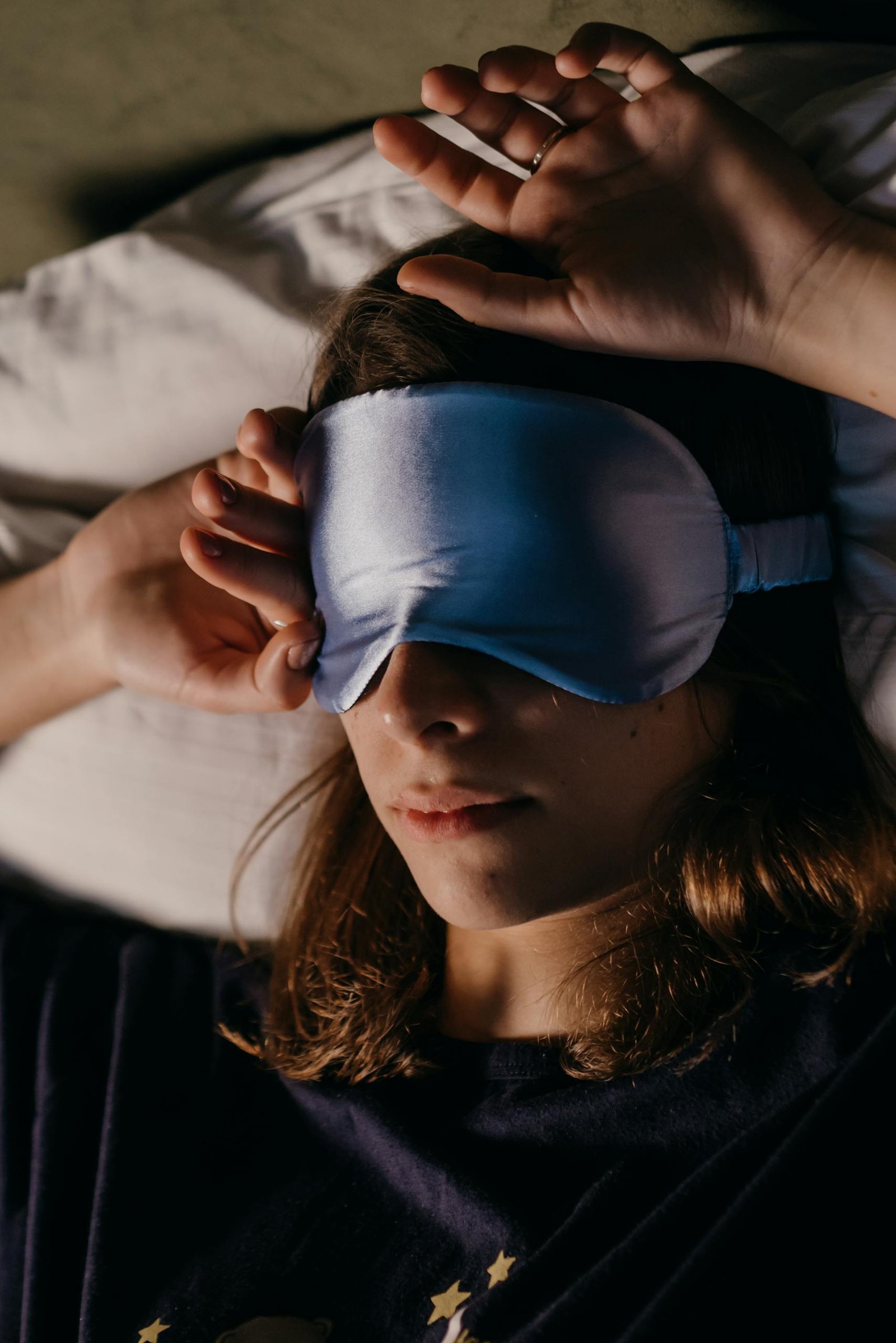 A woman enjoys restful sleep wearing a blue eye mask, serene and comfortable indoors.