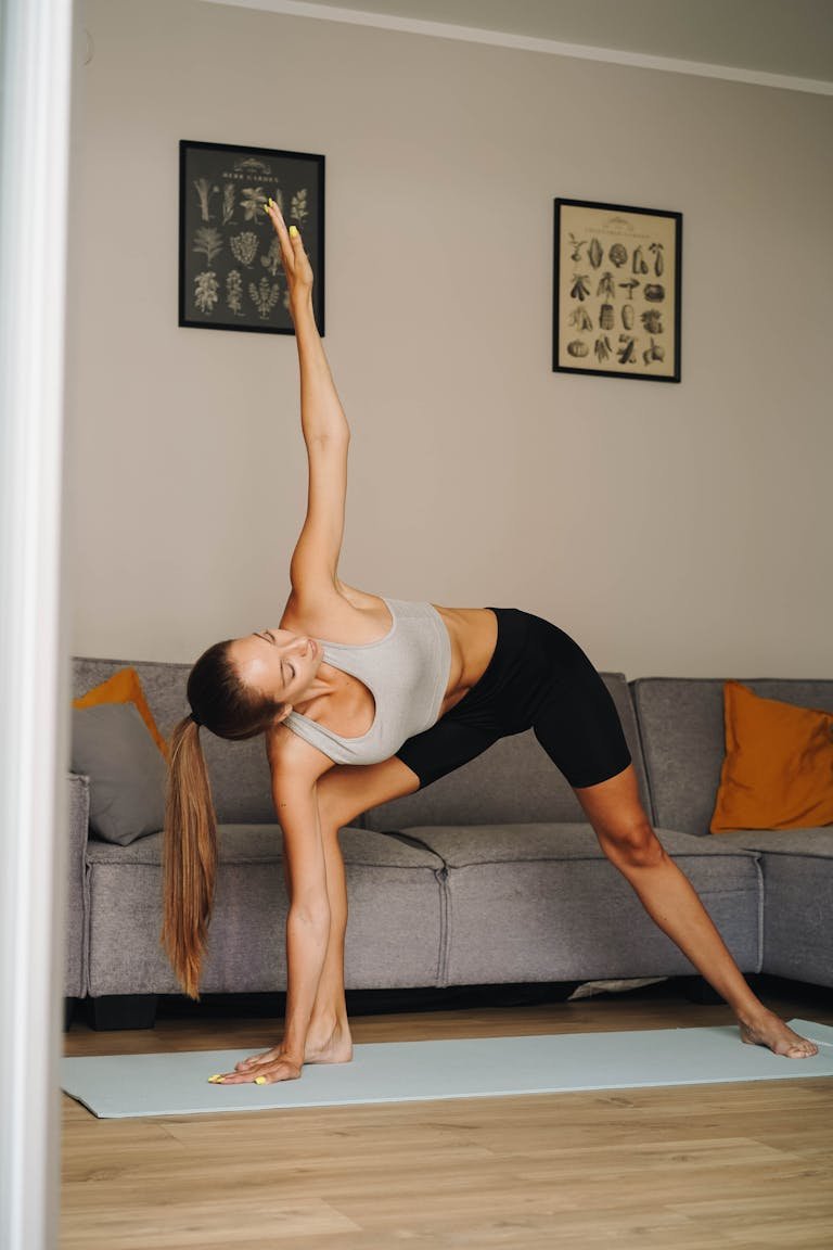 A woman in activewear performs the triangle pose on a yoga mat indoors, focusing on healthy lifestyle.