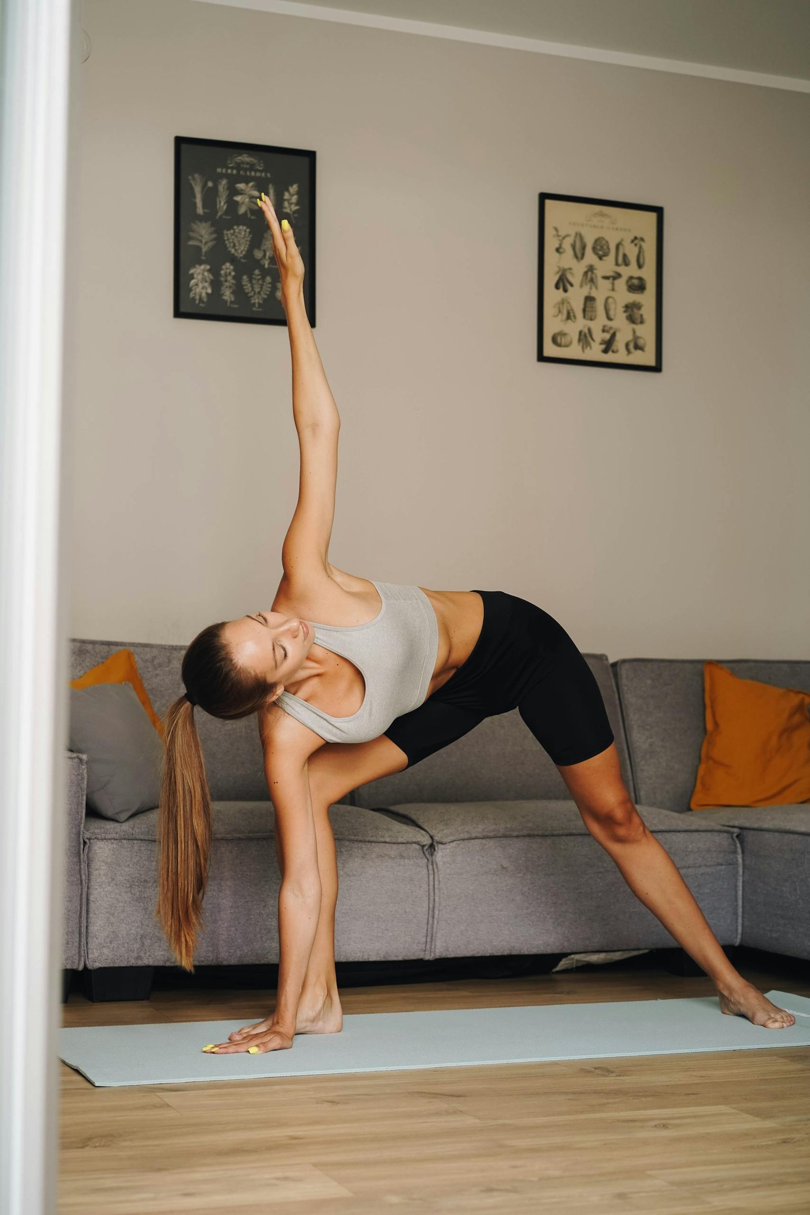 A woman in activewear performs the triangle pose on a yoga mat indoors, focusing on healthy lifestyle.